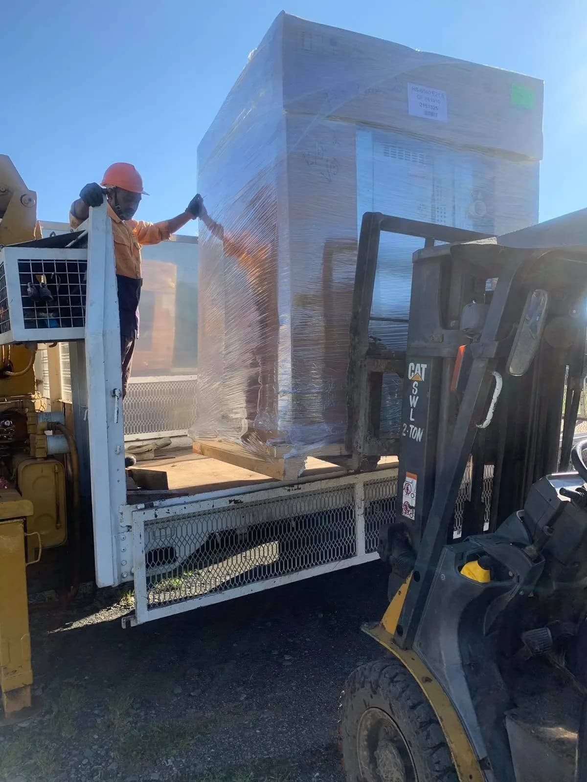 A forklift loading a packaged Girbau washer onto a delivery truck
