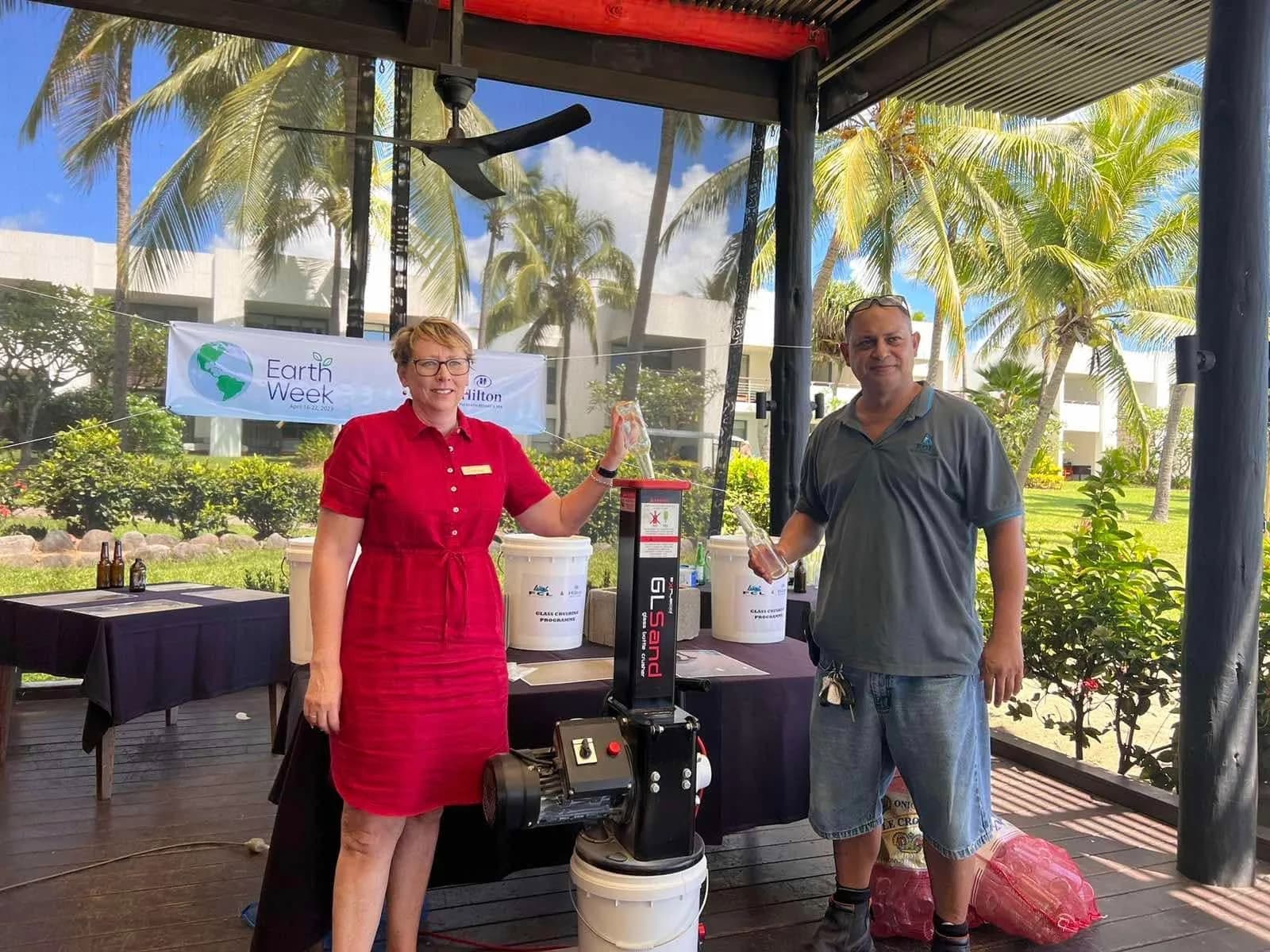 Fiji Chemicals and Hilton Fiji representatives beside a glass-crushing machine