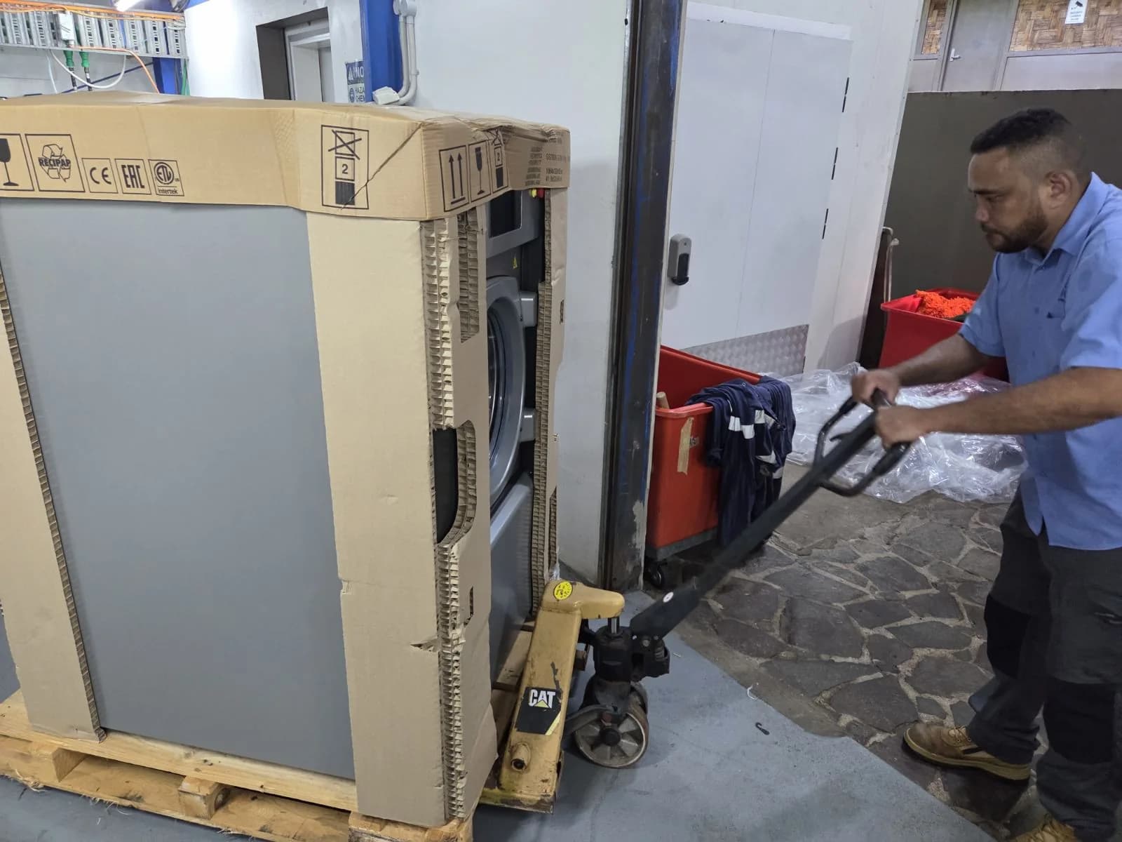 A Fiji Chemicals team member moving packaged laundry equipment with a pallet jack
