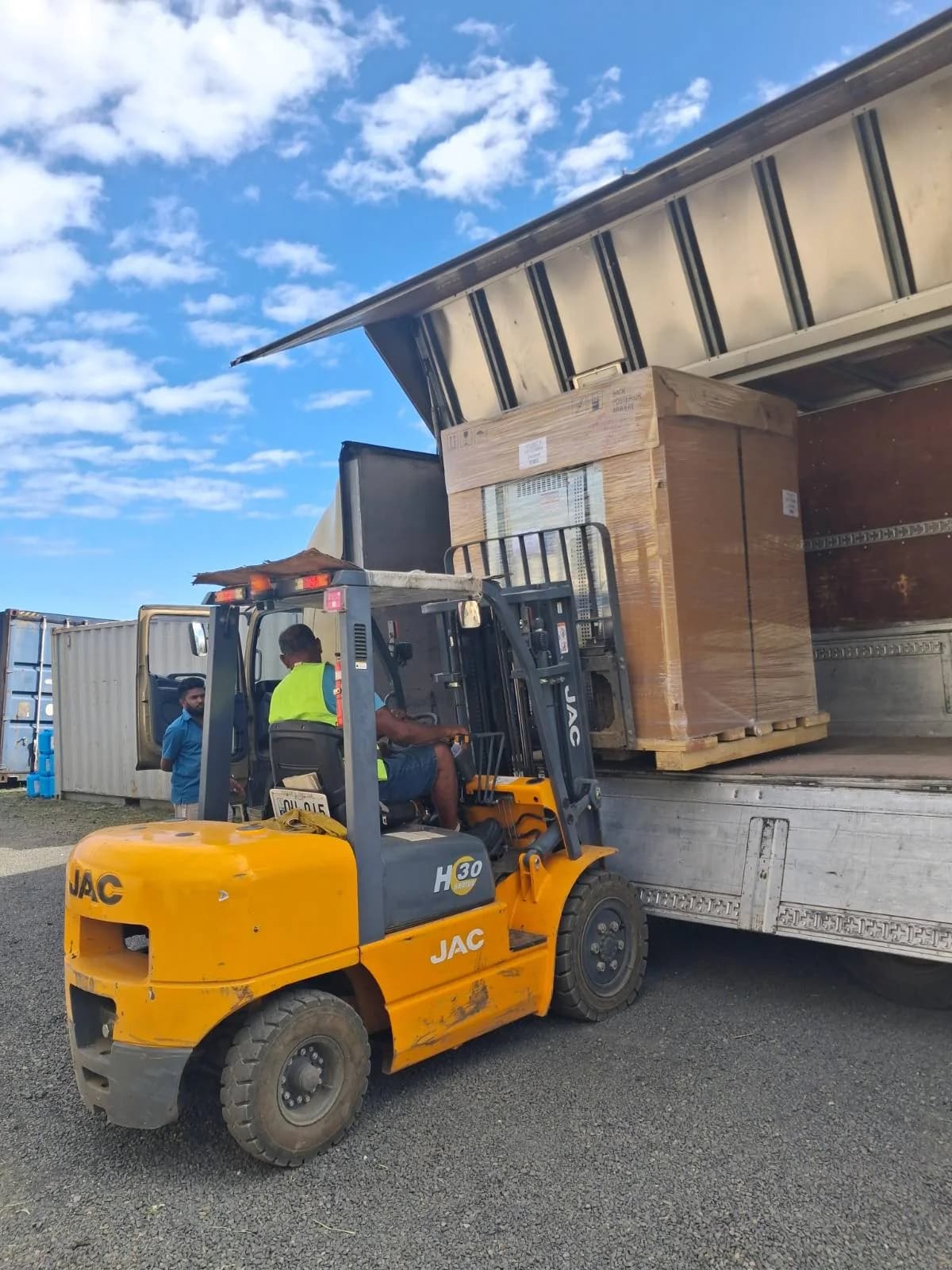 A forklift moving packaged equipment beside a delivery truck
